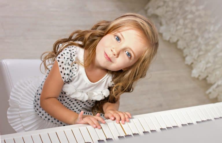 Beautiful little girl sits next to a piano