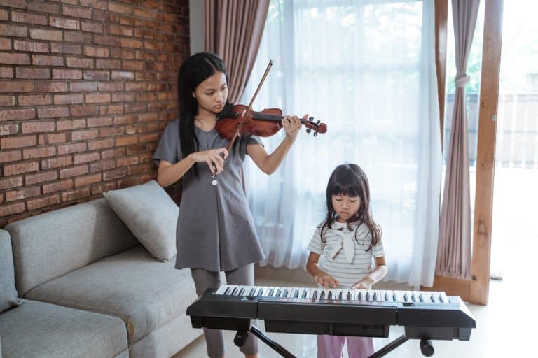 Little asian girl plays piano with her sister playing violin together